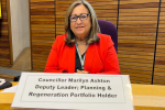 Cllr Marilyn Ashton sat in the old Council Chamber dressed in a red blazer looking at the camera and smiling. In front of her is her name plaque which reads 'Councillor Marilyn Ashton: Deputy Leader, Planning & Regeneration Portfolio Holder